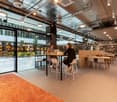 Modern office space with tables, chairs, glass walls, shelves, and carpet.