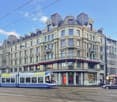 Large building with multiple floors, ornate architectural details, multiple windows, street tram in front