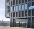 Modern office building with glass facade, entrance with glass doors, sign reading 'Grosspetertower', multiple floors, and a view of the city in the background.