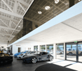 Open space with several luxury cars, modern interior, large windows, white ceiling, wooden floor