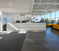 Car showroom with white reception desk, grey floor carpet, large windows, and luxury cars parked inside