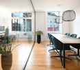 modern office, long table, chairs, glass wall, plants, white ceiling, white wall, monitors, desk