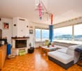 Spacious living room with large windows offering a scenic view, hardwood flooring, fireplace, sofa set, coffee table, and various decorative elements like colorful garlands and framed artwork on the walls.