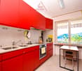 Spacious kitchen with red cabinets, granite countertops, sink, oven, and a small dining table with chairs. Large window overlooking the outdoor scenery.