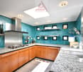 Spacious kitchen with teal-colored walls, wooden cabinets, granite countertops, stainless steel appliances including a dishwasher, and open shelving for storage and display.