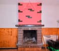 Brick fireplace with a large red abstract artwork above it, wooden paneled walls, various household items and tools in the room