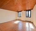 This image shows a spacious room with a wooden ceiling and hardwood floors. The room has large windows that provide natural light and a view of the outdoors. The walls are painted a neutral color, creating a clean and minimalist look. The room appears to