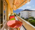 Red table and chairs, yellow wall, orange awning, large glass door, green plants, balcony view of a building and mountains