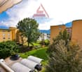 Outdoor area with parking shelter, trees, and a garden, overlooking the buildings and mountains in the distance.