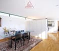 Glass table with four black chairs, wood floor, wall decorations, rug, cabinet with glass doors, white kitchen partition