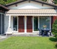 detached house, brown tiled roof, white exterior, awning, glass doors, table and chairs, grassy lawn, distant house, wooded mountain