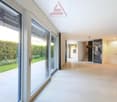Bright hallway with white tiles, glass doors, large windows, outdoor view of garden, well-lit with natural light