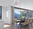 Dining room with large windows overlooking a mountain range, table with chairs, sofa, chandeliers, kitchen counter with glasses and plants