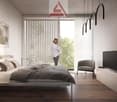 A bedroom with bed, pillows, flat screen tv, chair, and woman standing on a balcony looking outside.