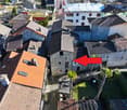 Stone house, terracotta roofs, multiple levels, narrow streets, surrounded by greenery, indicated by red arrow