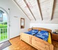 Bedroom with wooden bed, bedside tables, lamp, mirror, and sliding glass door.