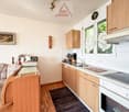 Modern kitchen with white countertops, wooden cabinets, an electric stove, oven, sink, and a coffee machine.