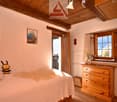 Bedroom with wooden bed, white bed sheets, bed spread, two stuffed toys, wooden cabinet, radiator, and window with vase and flower.