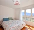 Bedroom with bed, pillows, nightstand, large windows, wooden floor, white walls, view of mountains and trees