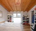 Bedroom with wooden floor, white walls, wooden ceiling, bed, wardrobe, shelves, books, picture frame, window, air conditioner
