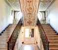 Ornate, grand staircase with intricate ceiling designs, marble steps, and decorative railings leading to a doorway at the top.