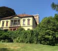 2-story yellow building with red tile roof, balconies, surrounded by lush greenery and trees