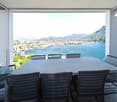 Large dining table with wicker chairs, overlooking a scenic lake and mountain landscape through large windows