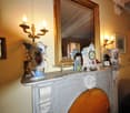 Ornate marble fireplace mantel with decorative vases and clocks, gilded framed mirror, wall sconces, and other antique decor items