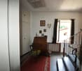 The image shows a living room with a wooden desk, framed artwork on the walls, and a fireplace. The room has a traditional, vintage decor with a red patterned rug on the floor.