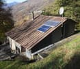 Mountain house with raised ground floor, solar panels on roof, surrounded by trees and grass