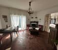 red tile floor, chandelier, fireplace, dining table, 2 red armchairs, windows with curtains, decorative items