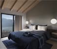modern styled room, wooden ceiling, gray walls, bed with dark bedding, bedside tables, large window with curtains, hanging lamps, view to outside, rug on the floor