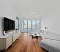 Modern living room with large windows, hardwood floor, gray sofa, coffee table, mounted television, floating entertainment center, ceiling light, scenic view