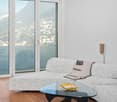 Modern design, light wooden floor, large windows, large L-shaped sofa, glass coffee table, artwork, scenic view