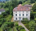 2 story house, brown roof, large windows, central door, multiple balconies, garden, path, trees