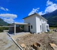 Two-story white house with a garage and parking space, surrounded by mountains and a blue sky with clouds