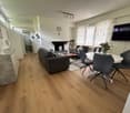 wooden floor, white walls, fireplace, gray couches, white table, flowers in vase, television