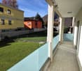 large glass balcony with transparent walls, tiled floor, grassy lawn below, buildings with balconies in background