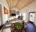 wooden ceiling, large couch, coffee table with plants, TV, potted plants, shelf with books and picture frames
