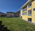 Yellow building with multiple windows, a grassy lawn in front, and a mountain in the background.