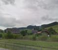Houses in a rural area, surrounded by trees and grass, with a cloudy sky