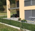 Apartment building, yellow facade, balcony, gate, yard with grass, grill, drying rack, fence