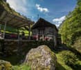 Stone cottage with wooden balcony, surrounded by greenery and mountains