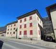 Large building with red shutters, several windows, steep slope roof, small car parked in front of the building