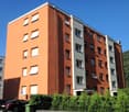 modern apartment building, orange exterior, white windows, fenced garden, mountain view