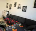 living room, white walls, black couch, decorative items, six picture frames, glass table, tiled floor, red rug