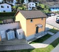 House located on a slope with two garages, one of which is attached to the house. There is a parking area on the side.