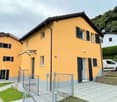 Yellow house, 2 floors, black roof, metal fence, garage, white windows, bushes and plants in the front, parked white van