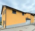 Two story house, yellow exterior, black shutters, gray trim, solar panels, garage, fenced driveway, view of mountains.