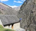 Stone house with solar panel on the roof, wooden door, surrounded by trees and mountains